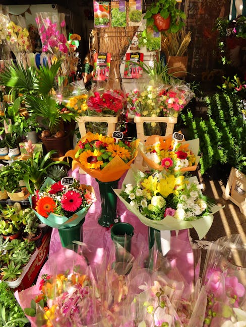 A display of fresh floral bouquets arranged on a pink table within a flower shop, featuring a variety of vibrant flowers including bright yellow sunflowers, pink gerbera daisies, white chrysanthemums,